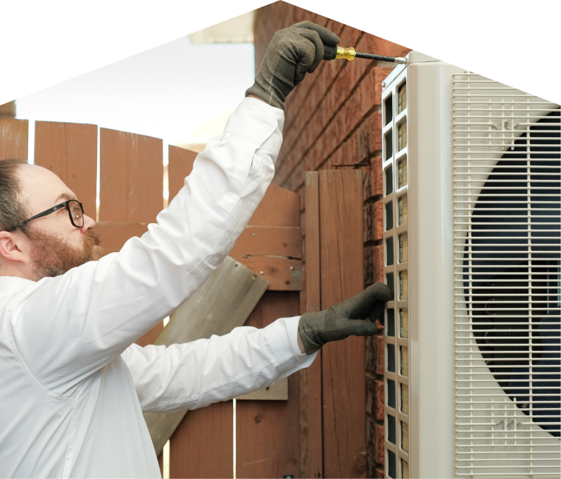 furnaceguys service personnel working on an AC condenser, using a screwdriver to secure the unit's panel outdoors beside a wooden fence.