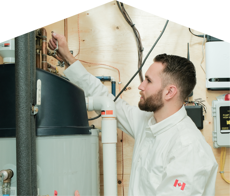 furnaceguys water heater specialist adjusts piping on a large residential unit during a repair service, with exposed wood paneling and mounted utility components in the background.